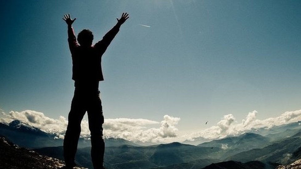 Man on top of a mountain, arms raised, sun rising