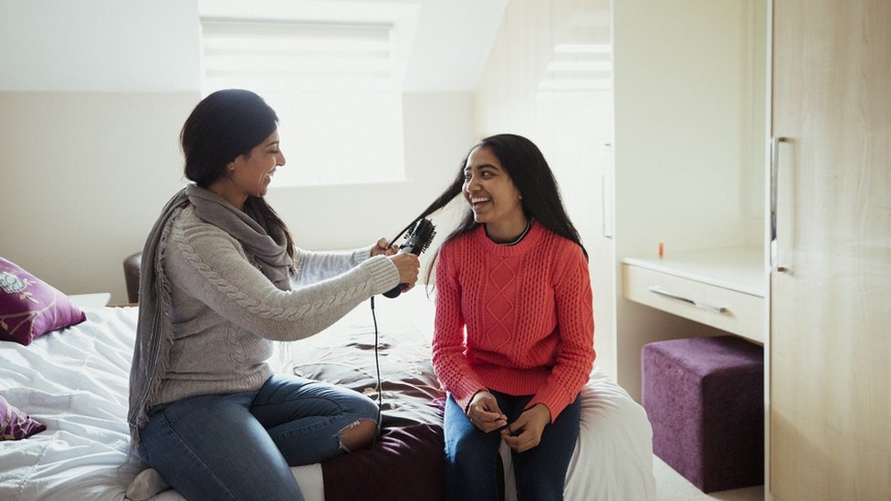 Mother and daughter, sitting on a bed, talking while combing hair