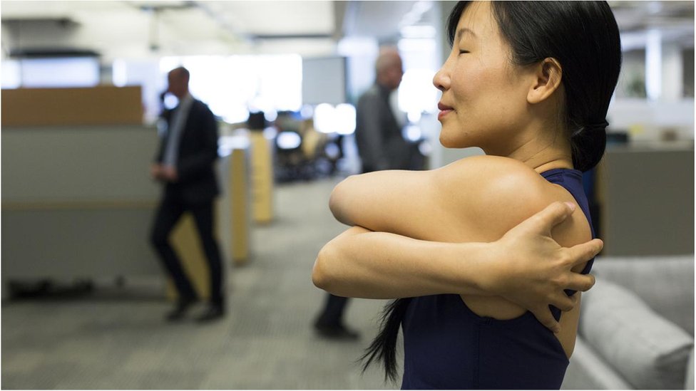 টরন্টোর একজন ফিটনেস প্রশিক্ষক অফিস কর্মীদের যোগব্যায়ামের কৌশল শেখাচ্ছেন।