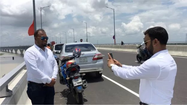 সেতুর উপর মোটরসাইকেল থামিয়ে ছবি তুলছেন দুই যাত্রী সেতুর উপর মোটরসাইকেল থামিয়ে ছবি তুলছেন দুই যাত্রী