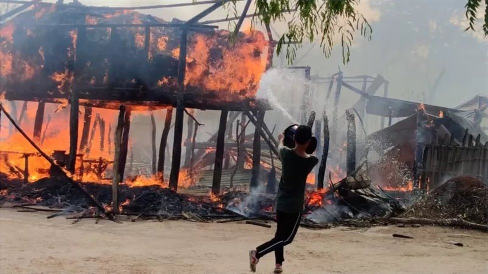 একটি জ্বলন্ত বসতবাড়িতে আগুন নেভানোর চেষ্টা করছে একজন একটি জ্বলন্ত বসতবাড়িতে আগুন নেভানোর চেষ্টা করছে একজন